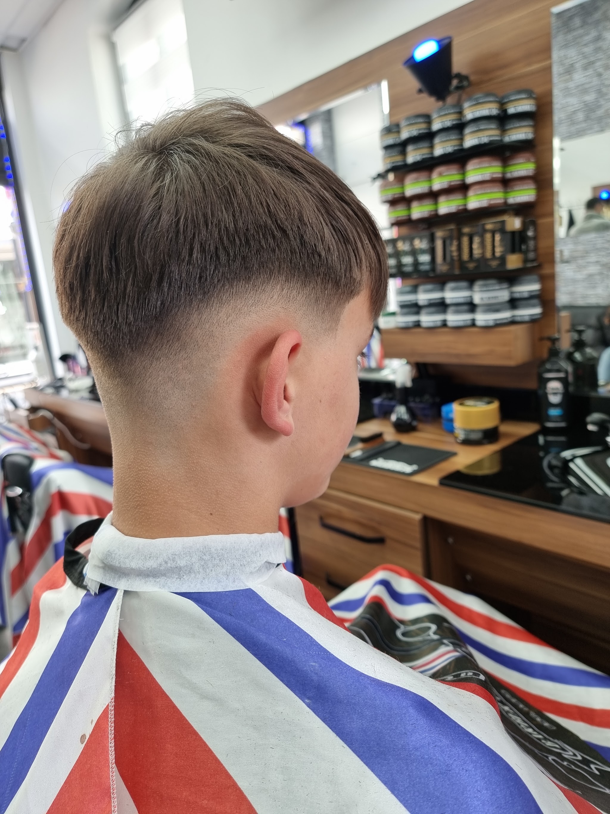 Jongen met een skin fade, in een rood-wit-blauw gestreepte kapmantel