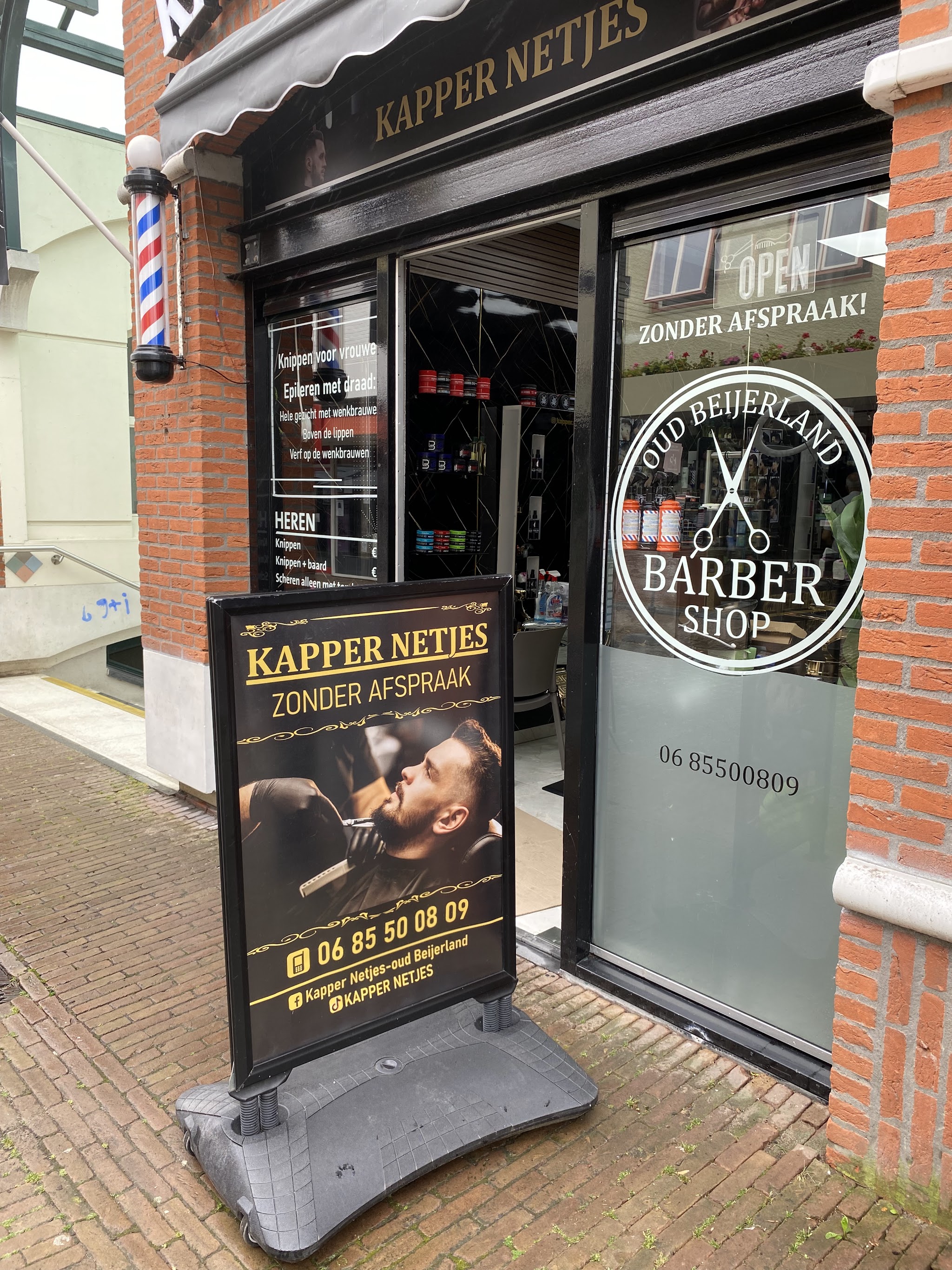 De winkel van Kapper Netjes met het stoepbord Zonder afspraak voor de deur en de barbierspaal aan de gevel