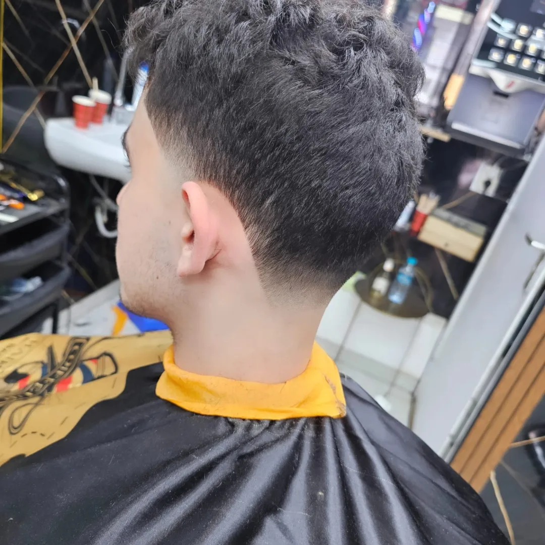 Low fade van achteren gezien, klant in een zwart met gouden kapmantel