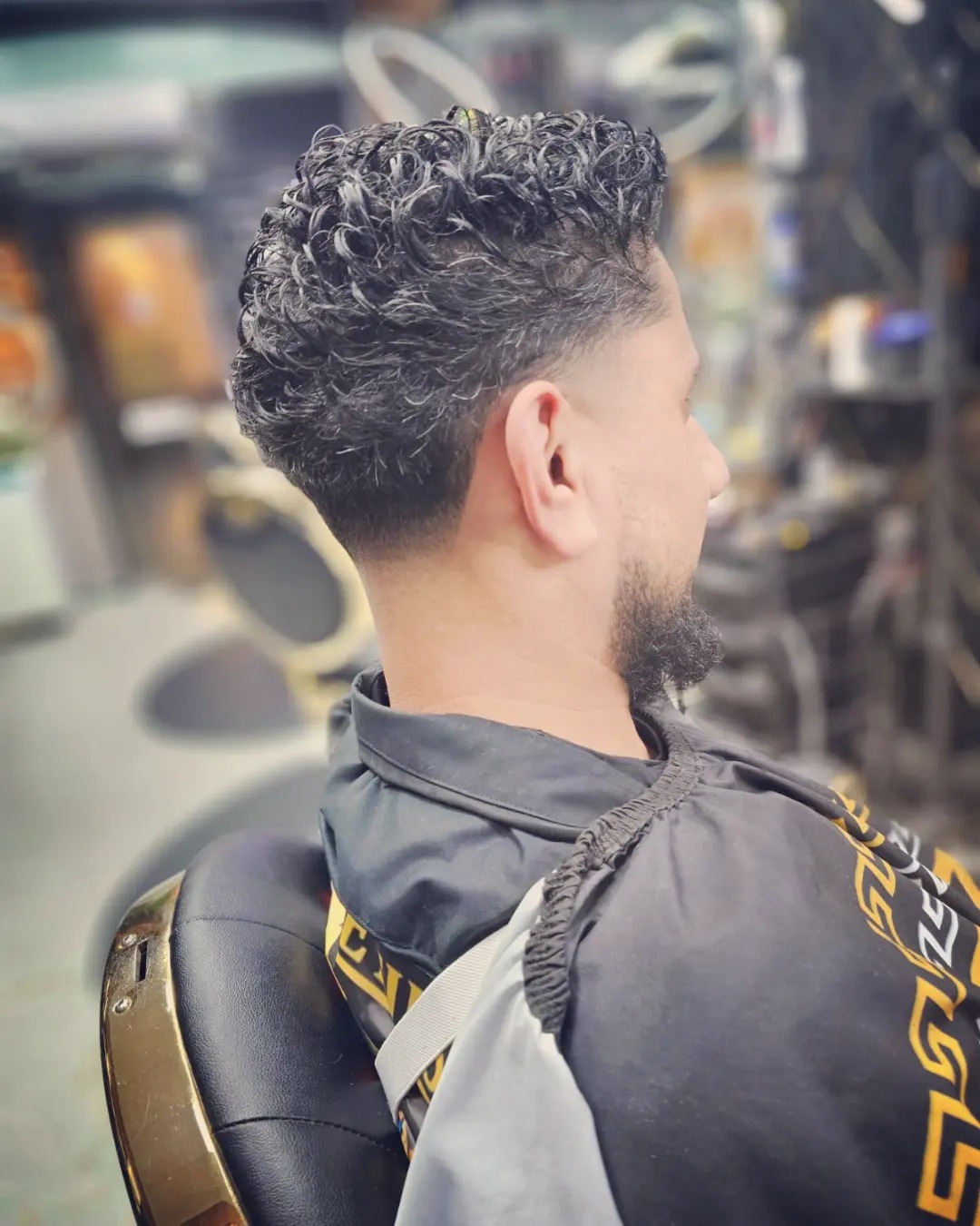 Krullend kapsel met fade en een verzorgde baard, zijaanzicht in de kappersstoel